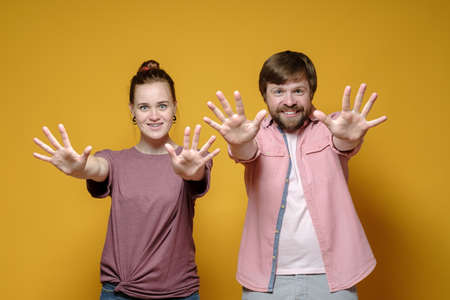 Cheerful, smiling woman and man show open palms, number ten and look happily. Yellow background.の写真素材