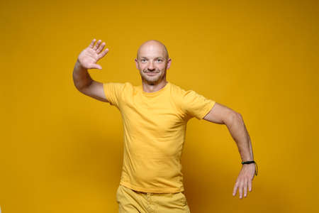 Funny bald, Caucasian man in yellow clothes stands with a bizarre pose and looks at the camera. Bright background.の写真素材