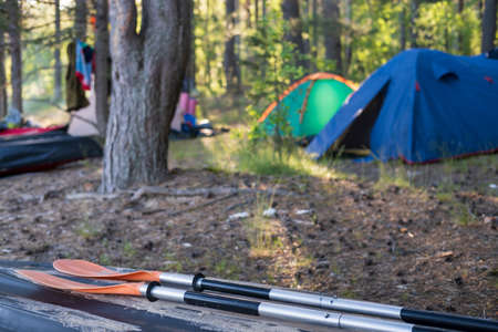 Oars lie on an overturned kayak on the shore, in the camp, against the backdrop of a tent and forest. Tourism and active lifestyle.の写真素材