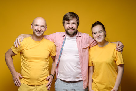 Friendly smiling bearded man hugs friends, man and woman. Yellow background.の写真素材
