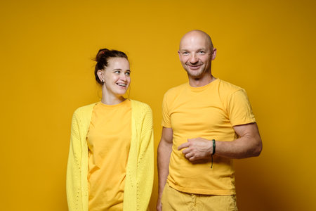 Young woman looks laughs looking at the smiling man. Positive emotions. Yellow background.の写真素材