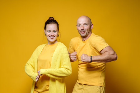 Funny man and woman stand in bizarre poses and strange faces. Positive emotions. Yellow background.の写真素材