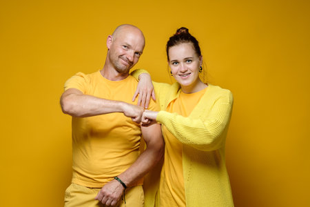 Cute smiling man and woman hug in a friendly way and make a peaceful gesture with their hands. Yellow background.の写真素材