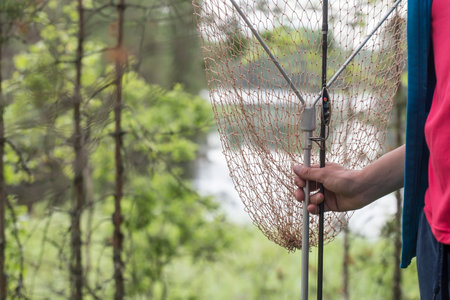 Hand holds a netting for pulling fish from the water, against the backdrop of a lake and trees, on a summer day.の写真素材