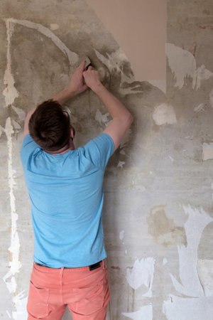 Home repairs. Man removes old wallpaper from the wall with a spatula.の写真素材