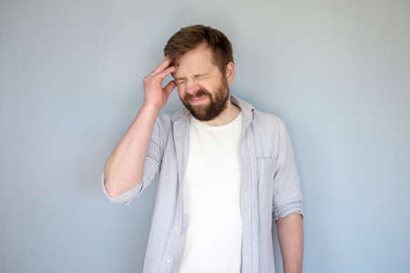 Young Caucasian man suffers severe headache or is trying to remember something, he touches his head and grimaces with closed eyes.の写真素材