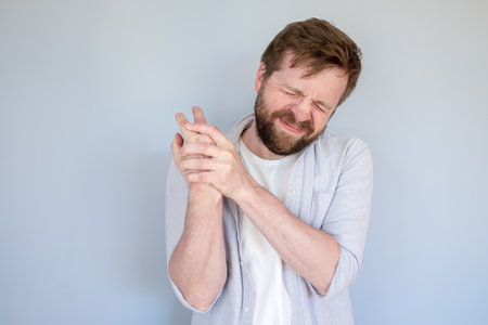 Bearded man experiences severe pain in arm, he massages the sore spot and closes eyes in suffering. Medical concept.の写真素材