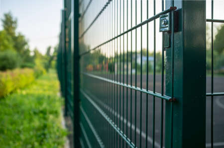 Sports ground is fenced with a green welded mesh fence, outdoors, in the evening at sunset.の写真素材