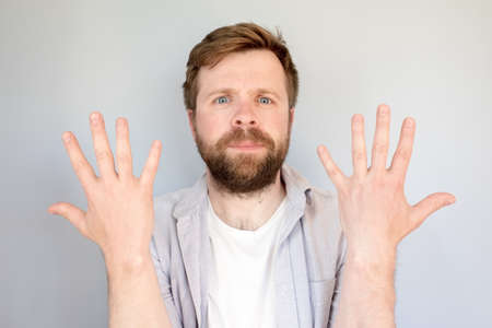 Contented, calm man in a shirt shows the number ten on fingers or his newly washed hands. Gray background.の写真素材