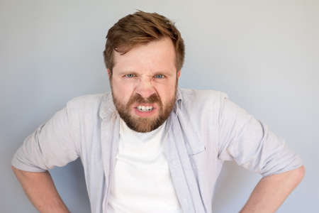 Caucasian bearded man is furious and displeased, he bares his teeth and looks angrily. Gray background.の写真素材