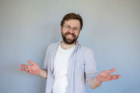 Friendly, charming man smiles cute and makes a gesture with hands. Gray background.の写真素材