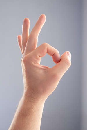 Male hand makes a sign ok, on a gray background. Fingers show okay.の写真素材