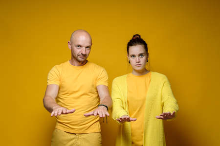 Serious, confident man and woman make a soothing gesture, put their hands forward and look sternly at the camera. Yellow background.の写真素材