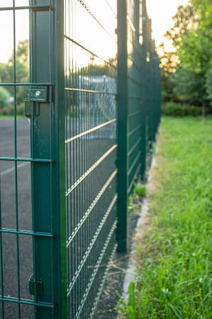 Sports ground is fenced with a green welded mesh fence, outdoors, in the evening at sunset.の写真素材