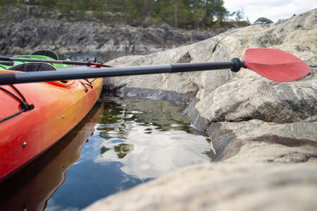Kayaks with oars are parked against the stony shore of the lake, against the backdrop of rocks, forest and sky. Open season. Leisure.の写真素材
