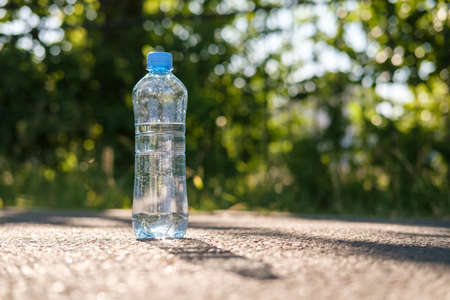 Bottle with clean cool water stands on the asphalt road in a summer hot day in the sun on a blurred background.の写真素材