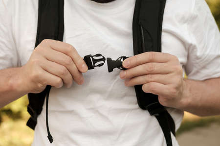 Man is fastening the plastic latch of a city backpack, which is worn on his shoulders. Close-up.の写真素材