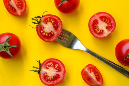 Red tomatoes and a fork lie on a yellow background. Beautiful picture. Sliced and whole vegetables with cutlery, top view.の写真素材