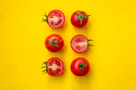 Red tomatoes, whole and sliced, isolated on a yellow background. Beautiful picture. Top view.の写真素材