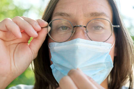 Woman wearing foggy glasses due to wearing a medical mask. Inconvenience due to condensation on the lenses. Close-up.の写真素材