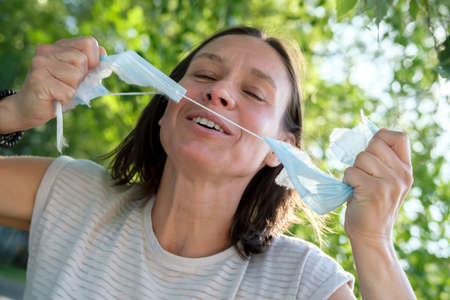 Joyful woman tears the medical mask on her face, she smiles and feels free. Concept of defeating the virus, the end of the pandemic.の写真素材