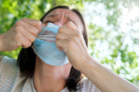 Woman emotionally tearing medical mask from his face, she gasps and tired. Concept of freedom and the end of the pandemic.の写真素材