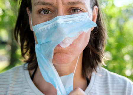 Portrait of an unhappy, tired woman in a torn medical mask. Concept of defeating the virus and ending the pandemic.の写真素材