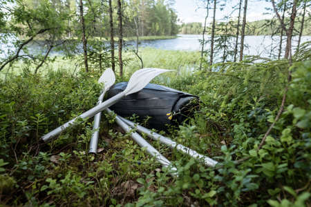 New rubber inflatable boat and oars lie in the grass, on the shore of the lake. Preparing for a boat trip or fishing. Active lifestyle.の写真素材