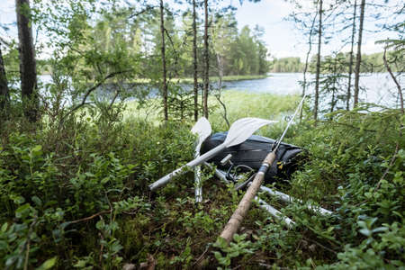 New rolled up rubber inflatable boat, oars and a spinning rod lie in the grass, on the shore of the lake. Preparing for fishing.の写真素材