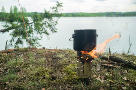 Bowler with cooking food stands on a metal, portable burner from which there is a flame, from the burning wood, on a rock.の写真素材