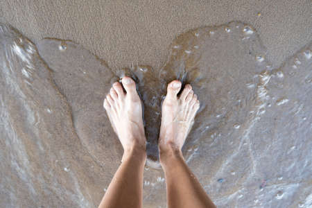 Women tanned legs stand in the water, on the sandy bank of the river, on a summer day. Lifestyle. Top view.の写真素材