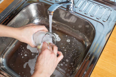 Women hands wash a glass, using detergent and a sponge, in the sink under running water in the kitchen. Housework.の写真素材