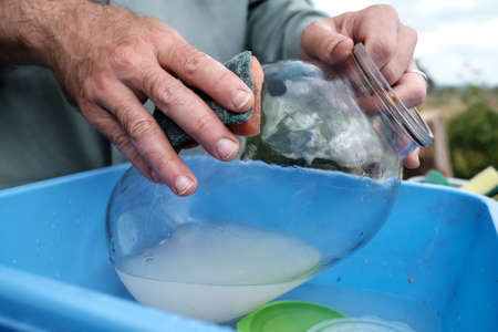 Male hands wash a dirty glass jar with a sponge, in a plastic basin, in a village courtyard, outdoors. Rural traditions.の写真素材