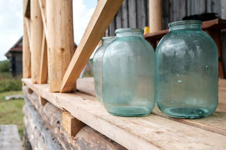 Dirty glass jars standing on a wooden porch of a village house, in the yard.の写真素材