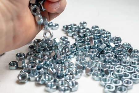 Hand of a male mechanic scattering new, shiny screw like jewels on a white table.の写真素材