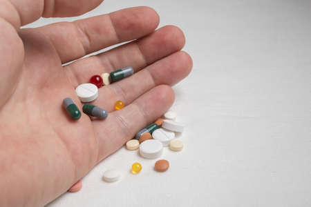 Bright, various medicinal pills wake up from a man palm on a white table.の写真素材