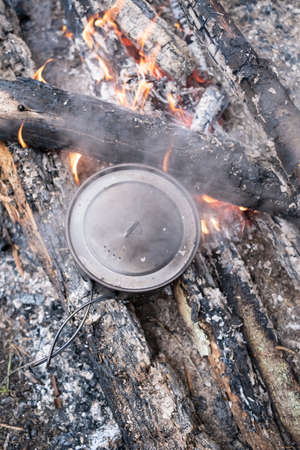 Pot of preparing food stands on the coals campfire, camp, summer day. Top view.の写真素材