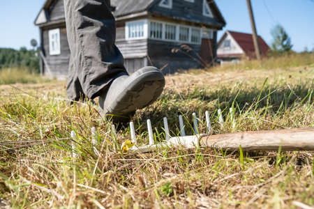 Leg of a careless, inattentive man steps on a rake, which can lead to injury, against the backdrop of a village house. Bottom view.の写真素材
