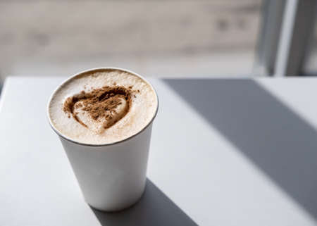 Cappuccino with cinnamon and a painted heart on lush foam, in the rays of the sun. Invigorating, aromatic morning drink. Copy space.の写真素材