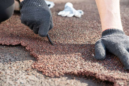 Male hands in gloves are repairing the sports ground, cutting out the damaged area of the special coating with a knife.の写真素材