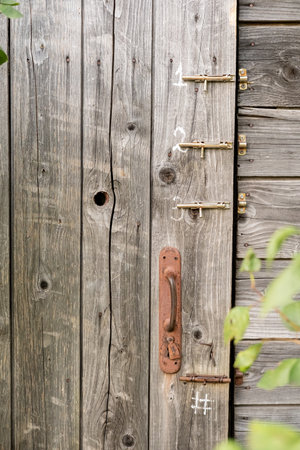 Door of an old wooden toilet or barn with a rusty doorknob and three latches, in a countryside.の写真素材