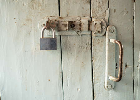 Painted, dirty wooden door with metal handle, latch and padlock, in a country house.の写真素材