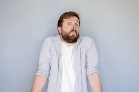 Bewilderment bearded man in a shirt shrugs in surprise and looks at the camera with a strange and funny expression on face.の写真素材
