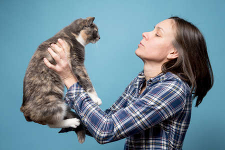 Woman in a shirt holds her adorable cat in her hands and looks at her attentively. Concept of playing and taking care of pets.の写真素材