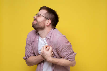 Caucasian bearded man is experiencing severe pain in the heart, holding his chest with his hands with his eyes closed.の写真素材