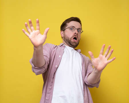 Caucasian man is frightened and in bewilderment, he makes a stop-gesture, holding out palms, and looks with apprehension.の写真素材