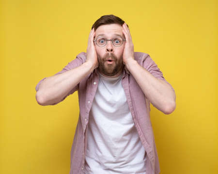 Bearded man with glasses is surprised by an unexpected surprise, he looks in bewilderment and holds...