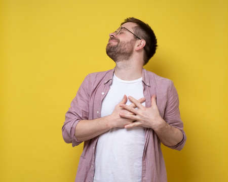 Charming, romantic man is in love, he holds hands on chest in the area of the heart and closed eyes dreaming and anticipating happiness.の写真素材
