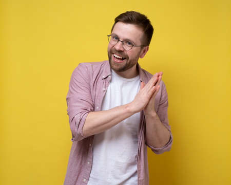 Positive, charming man clasped hands together, looks at the camera happily and smiling. Yellow background.の写真素材