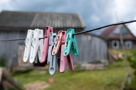 Plastic clothespins hang on clotheslines, in a rustic courtyard, against the backdrop of a wooden barn and the sky.の写真素材